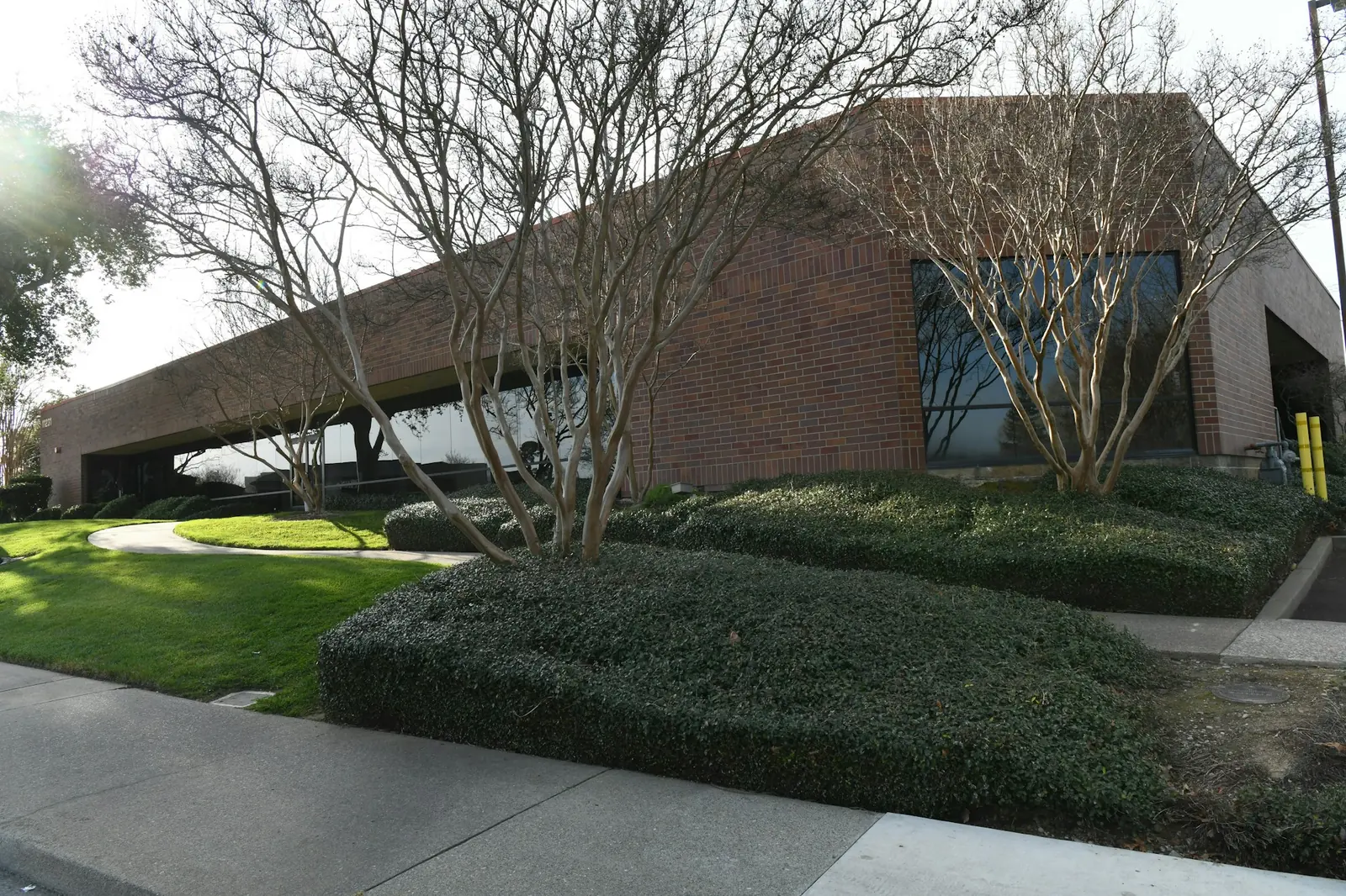 Maintained shrubs, lawn, and walkways outside a brick office building