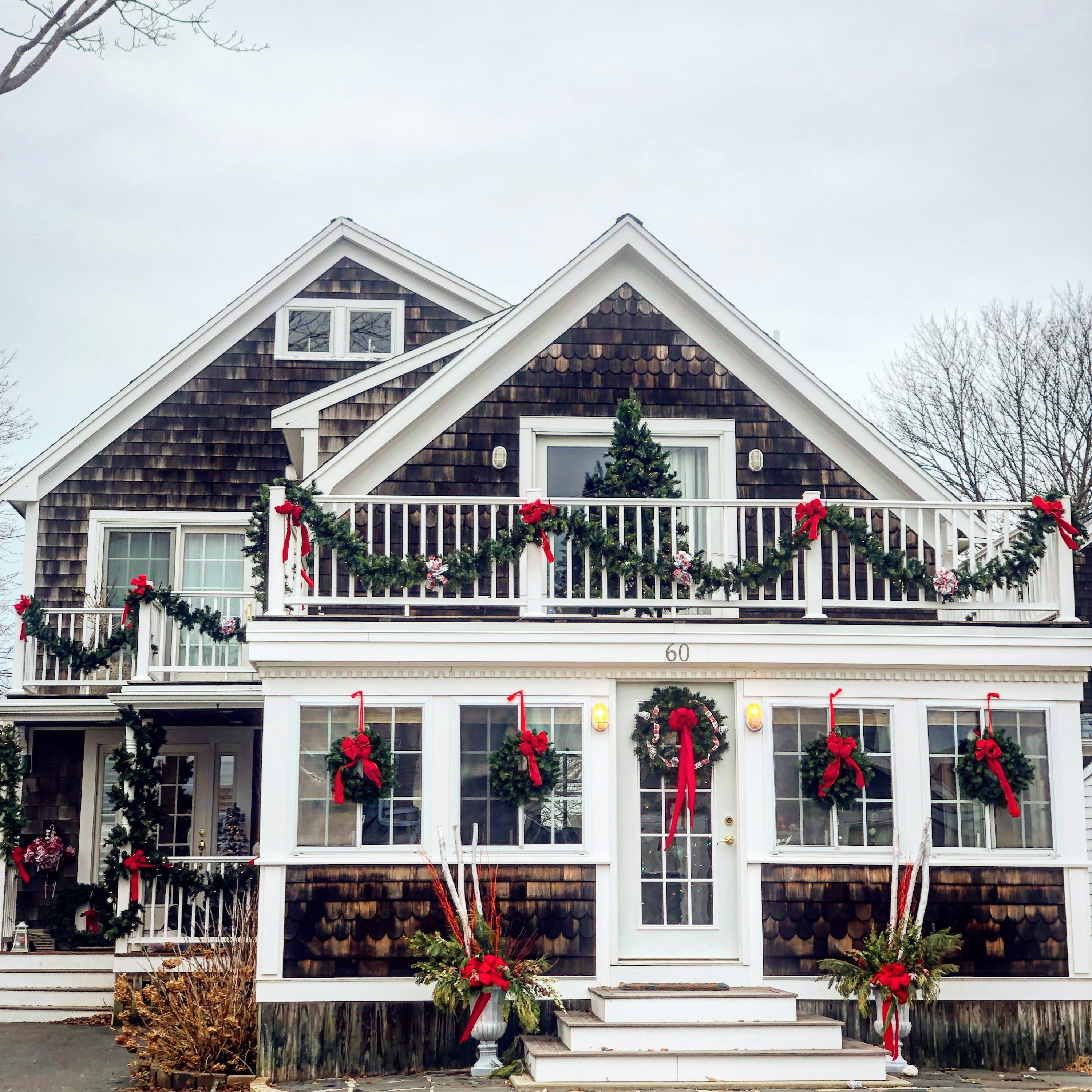 Holiday styling inspiration: a shingled home with evergreen garland, red bows, wreaths and decorated planters