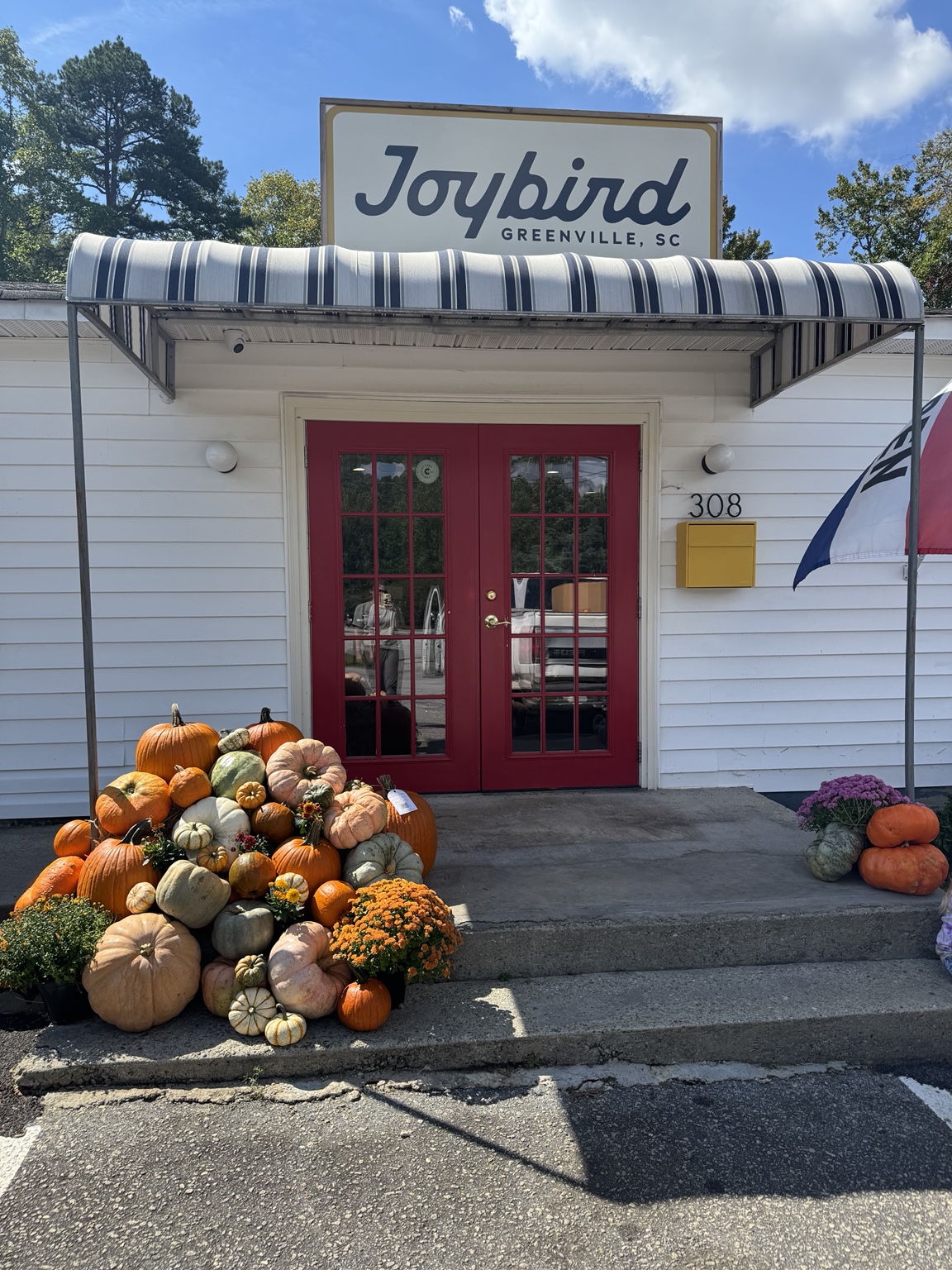 Completed Seasonal Porch installation with orange, pale green and white pumpkins, gourds and mums beside a red doorway
