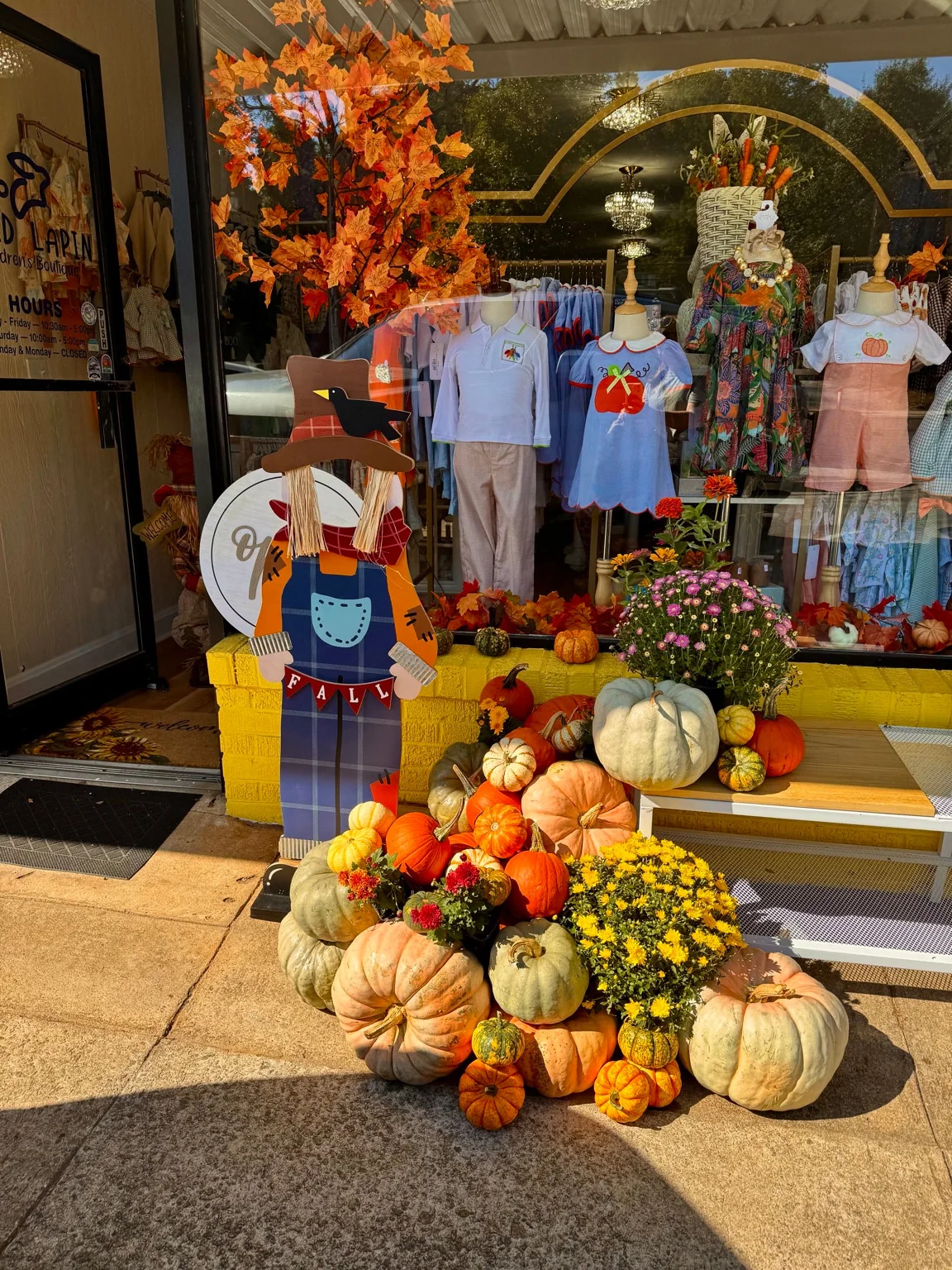 Layered orange and pale green pumpkins, gourds and mums outside a boutique window
