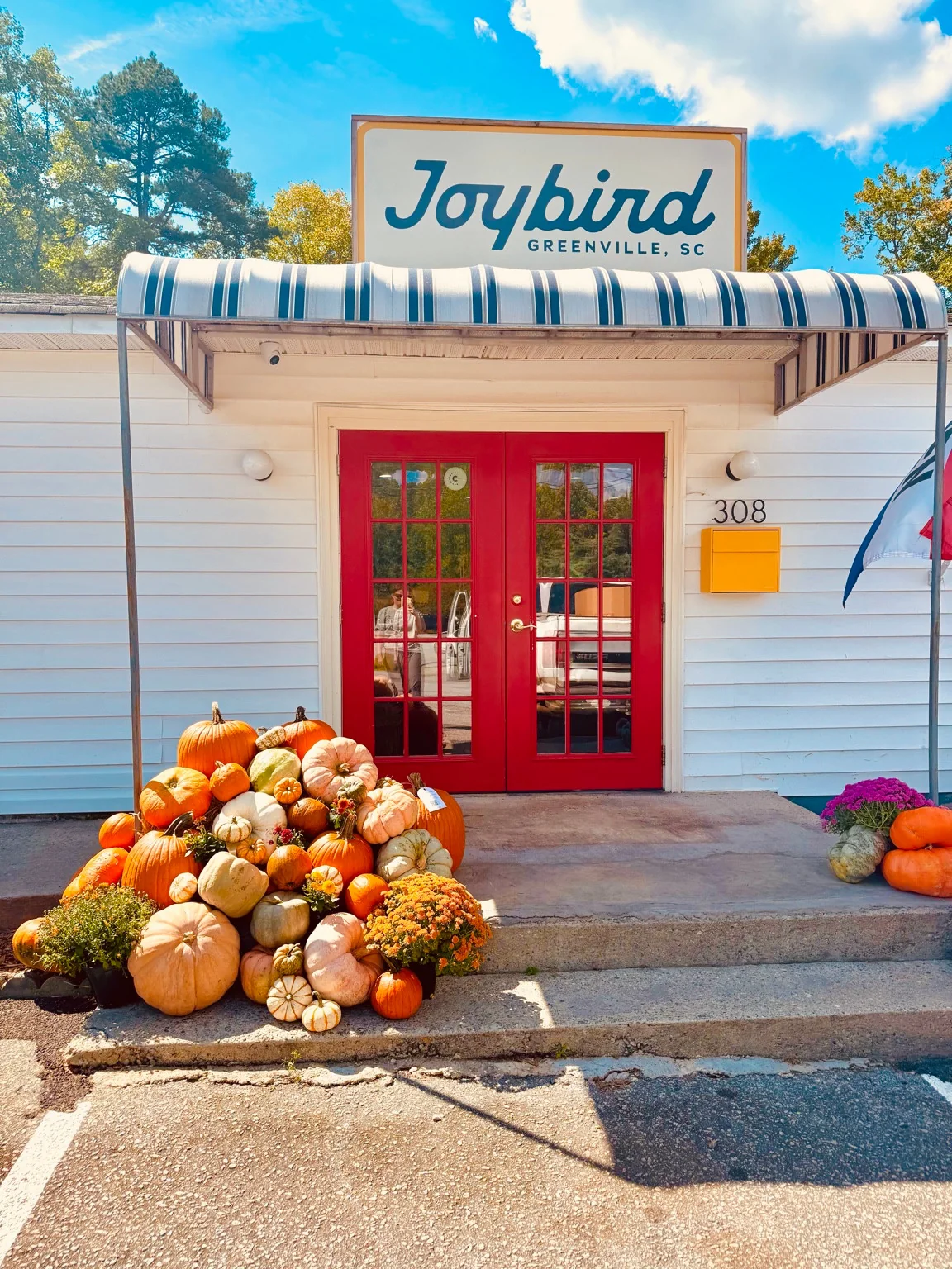 An abundant pumpkin, gourd and mum display beside the red doors of a storefront
